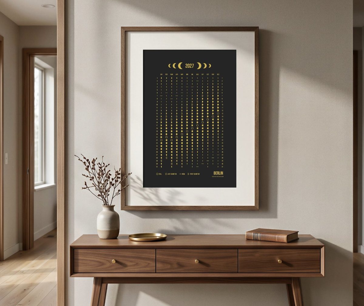 A yearly moon phase calendar for Berlin, gold on black, framed above a walnut console table